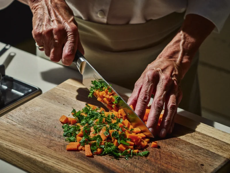 Mani di una persona anziana tagliano verdure su un tagliere